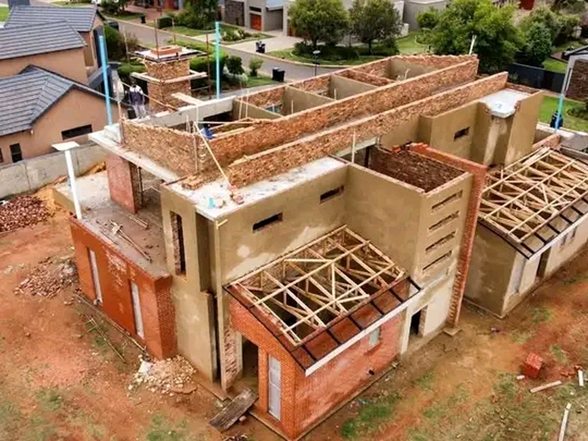 Two-story brick house under construction with exposed roof truss framework