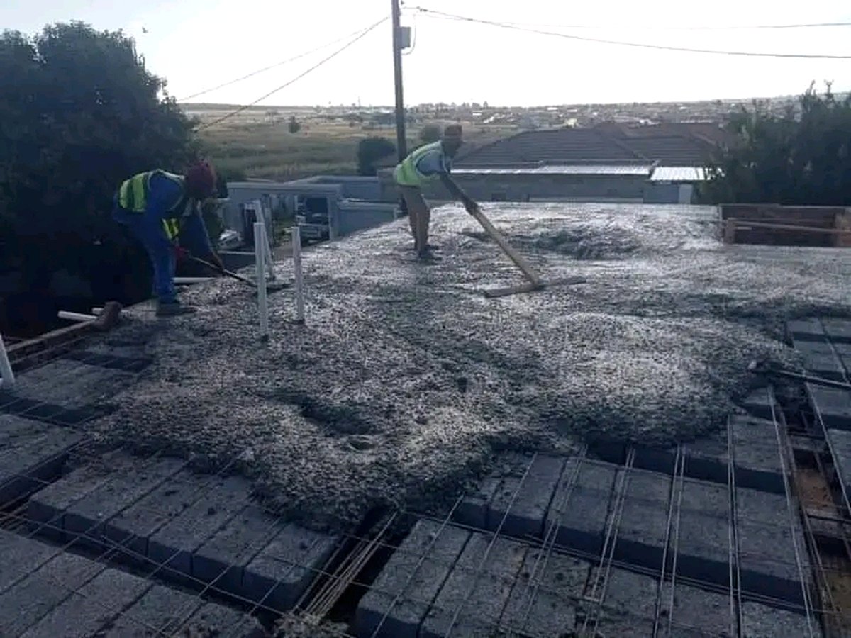 Workers smoothing wet concrete on roof surface with wooden floats