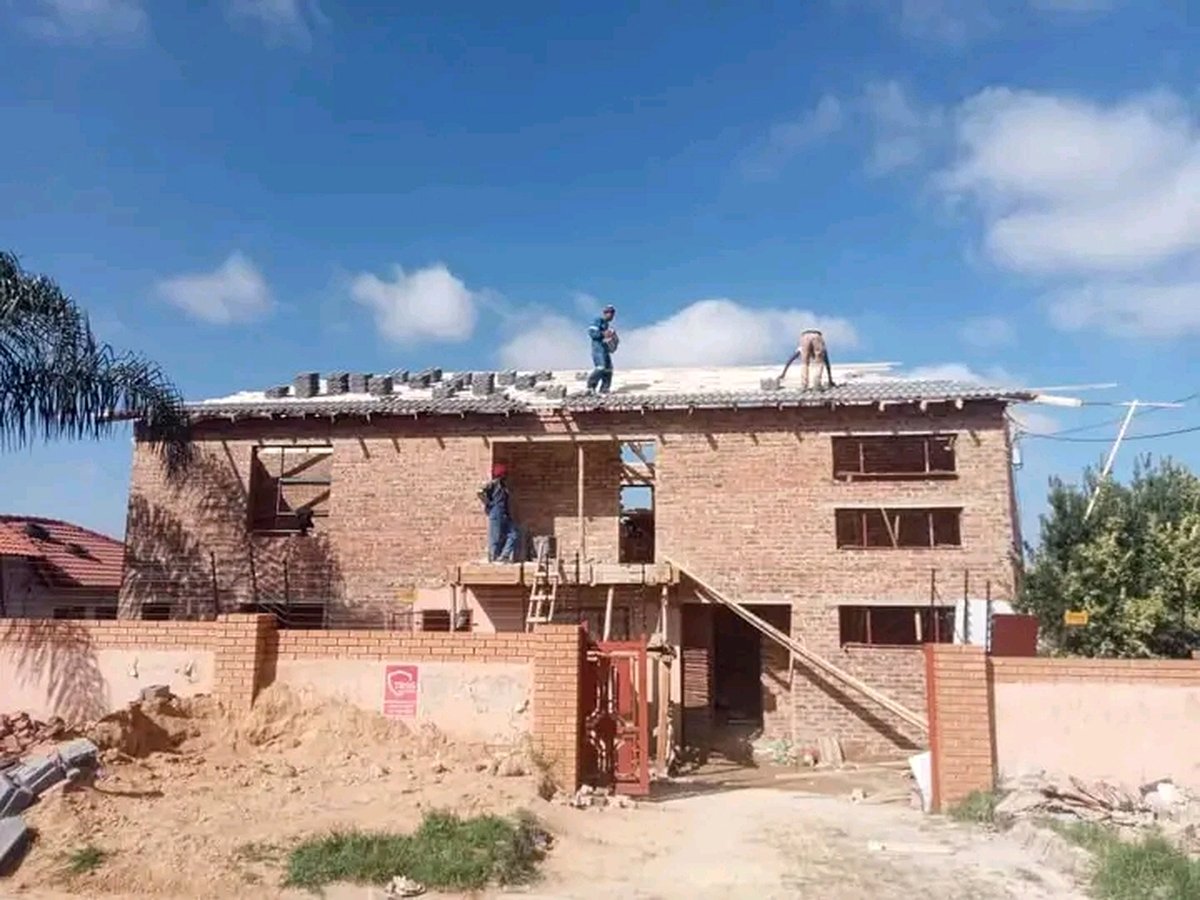 Workers installing roof tiles on two-story brick house under construction