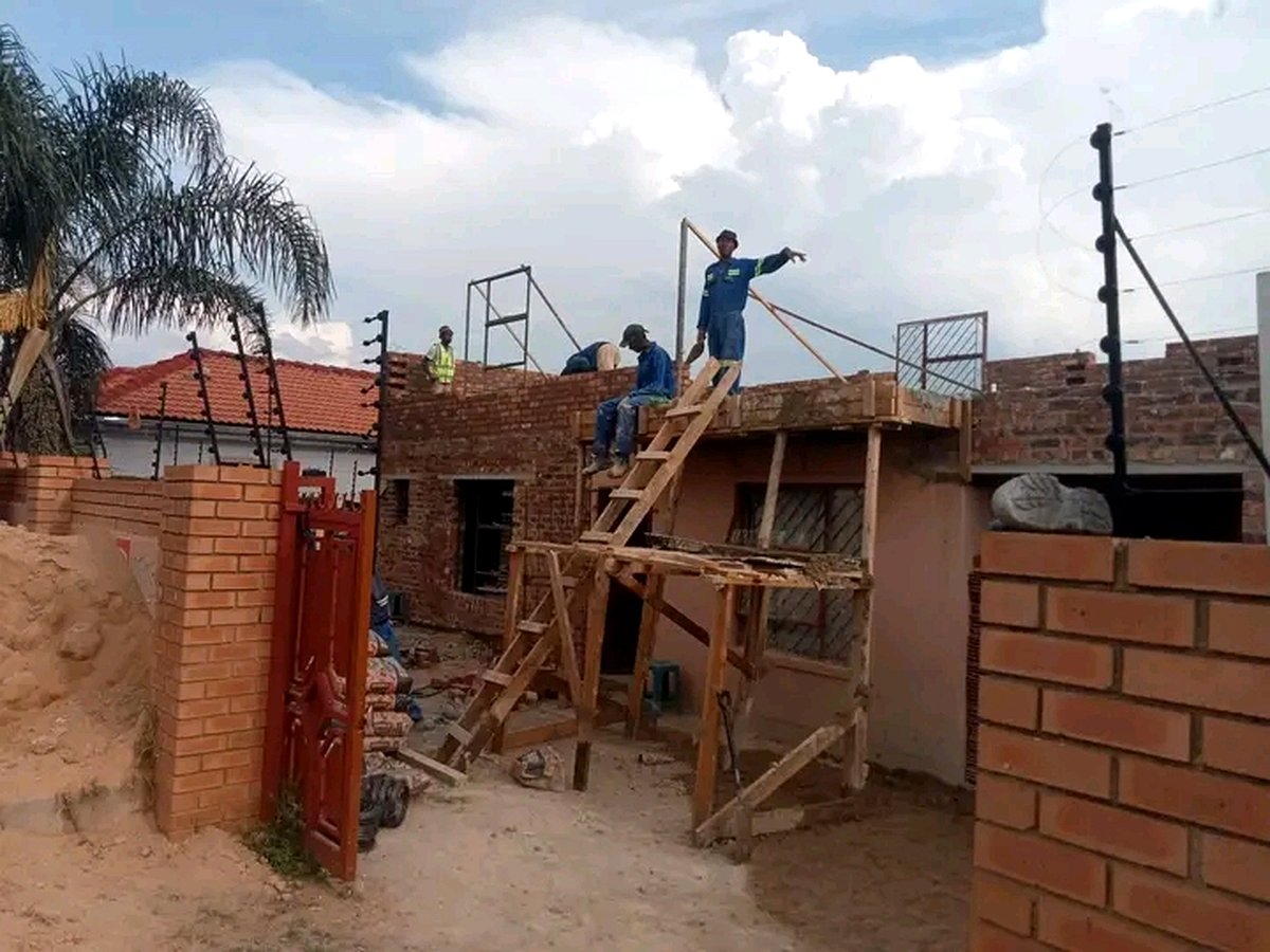 Workers on scaffolding and ladders building brick walls on construction site